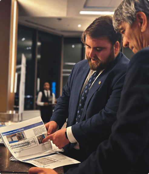Two men in business attire review a strategic document at a conference table, with a focus on the younger man pointing at the paper.