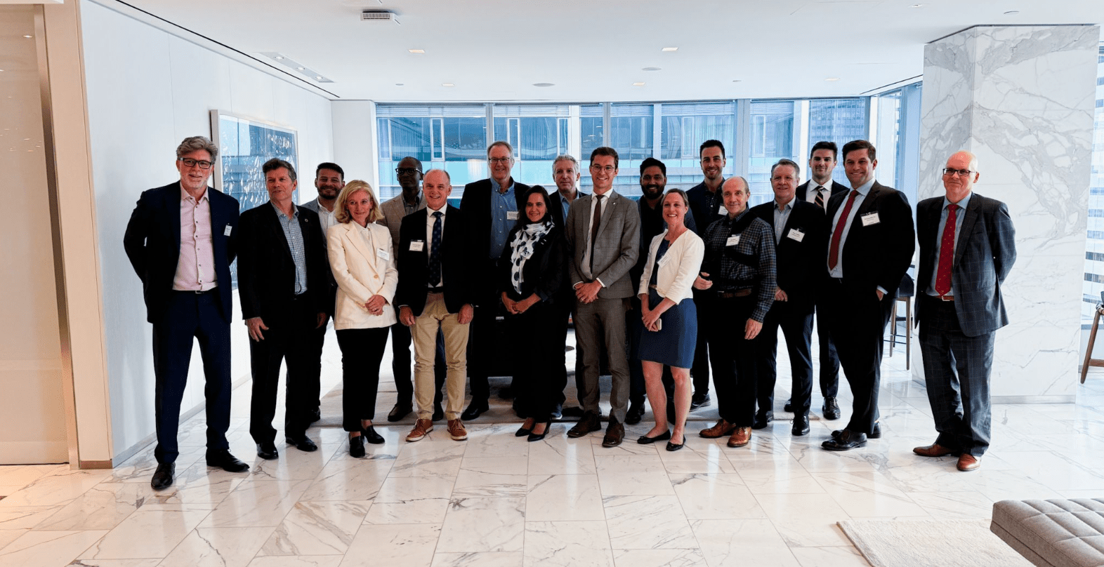 A group of sixteen people dressed in business attire stand together in a well-lit office space with marble flooring and large windows, gathered for a roundtable discussion on Ontario’s hydrogen sector.