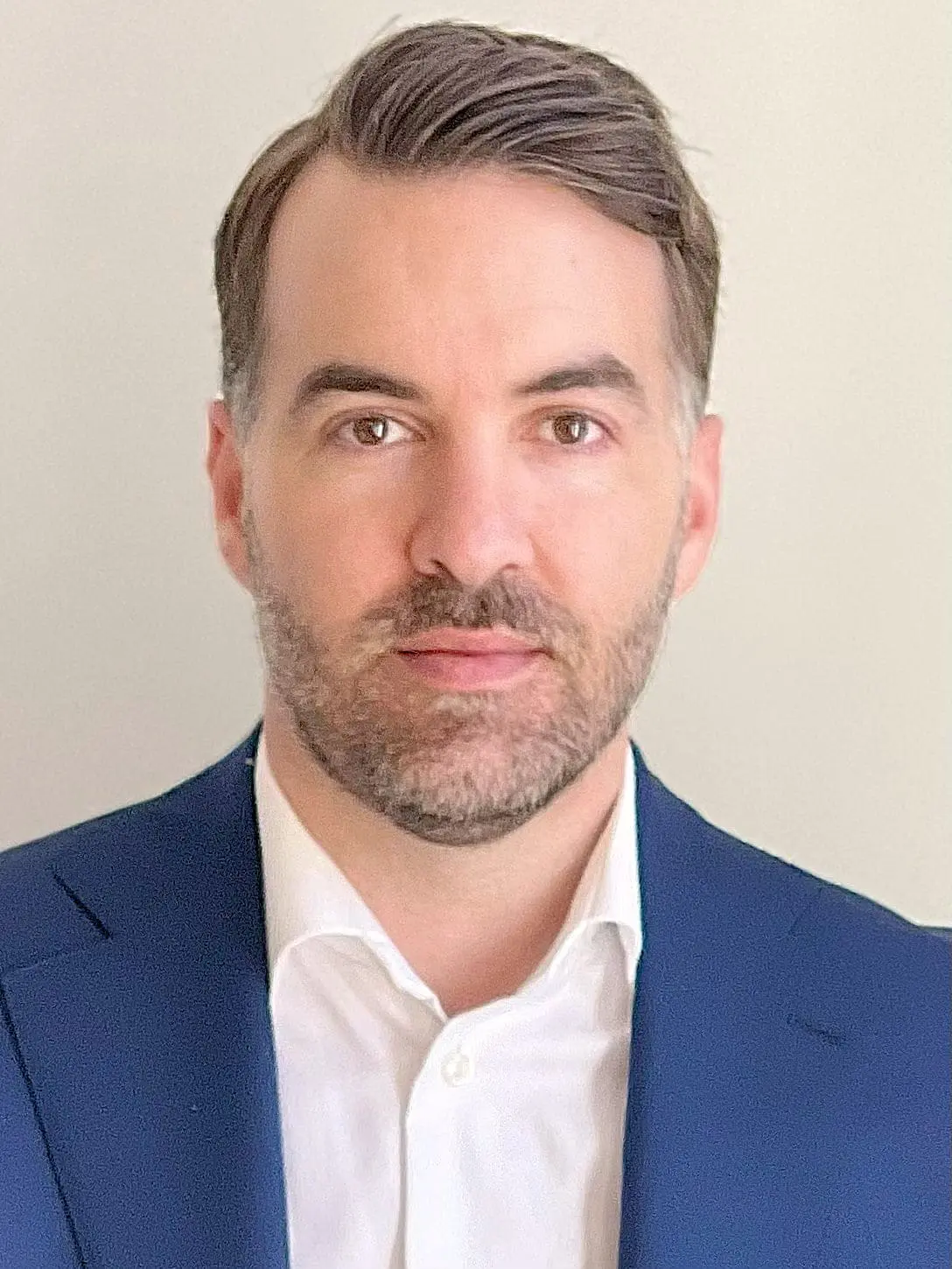 Jean-Francois Fournier, a man with short dark hair and a beard, wearing a navy blue suit jacket and white shirt, poses in front of a plain light background.